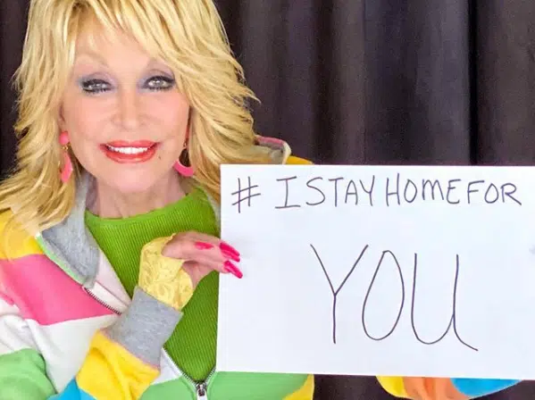 Dolly Parton holding a sign that says, "I stay home for you" stays home