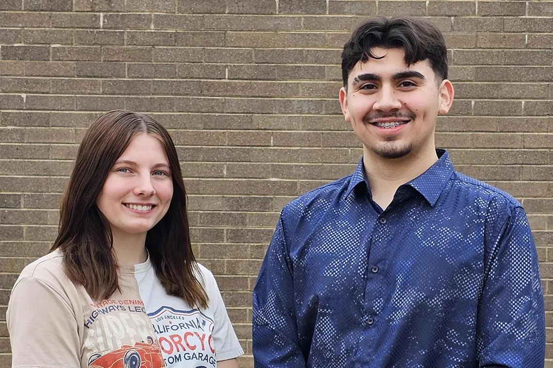 two high school student pose in front of a brick wall