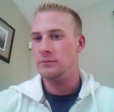 John Keyler with blonde tipped crew cut hair, wearing a white zip up hoodie overtop of a a dark blue t-shirt