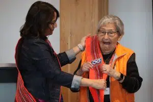 MNA President Andrea Sandmaier giving an Orange Sash to Residential School Survivor Angie Crear at Metis Crossing (Photo Credits - Daniel Barker-Tremblay)