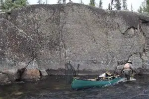 Calem Watson walking through a stream dragging his canoe with him in the Northwest Territories