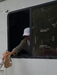 A woman wearing a hat hands a bagged lunch out the window of a truck to a child